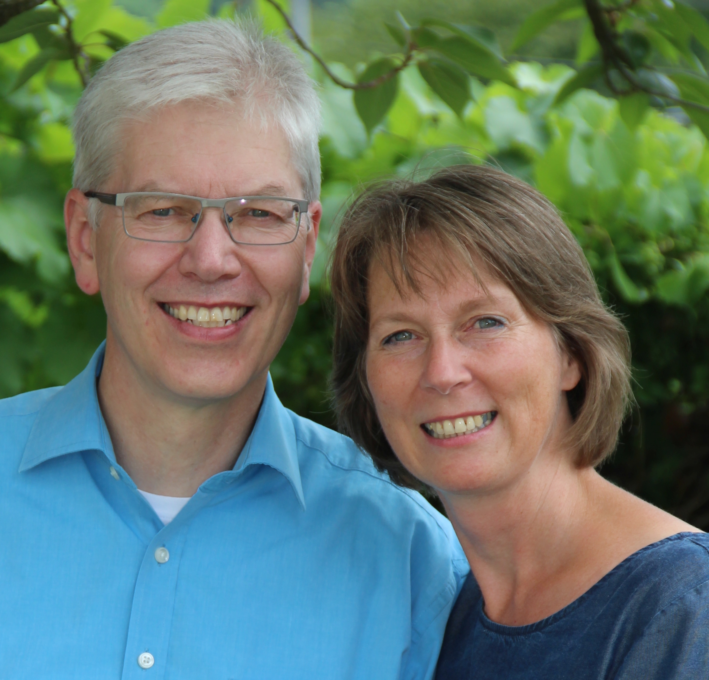 Sabine und Peter Piekenbrock lächeln gemeinsam vor grünem Blätterhintergrund